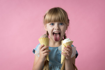 little girl with pigtails in a blue dress eating ice cream in a cone on a pink background