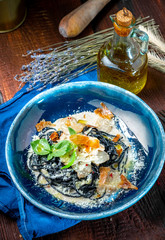 Pasta Carbonara with black spaghetti with squid ink with bacon and Basil on a blue plate - gastronomic experiments