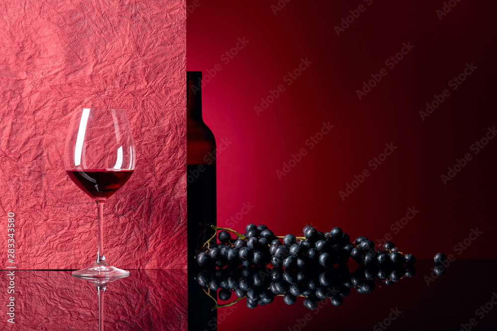 Wall mural bottle and glass of red wine on a black table.