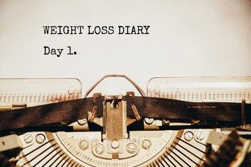 Wight loss tracking concept. Close up typewriter mechanism with a paper sheet and text "Weight loss dairy. Day 1". Closeup. Vintage look.