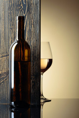 Bottle and glass of white wine on a black table.