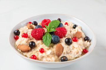 oatmeal porridge with fresh berries, nuts, honey, mint in a bowl for healthy diet breakfast