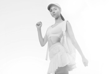 Fototapeta premium Sports woman posing in fashion sportswear on sunny sky background. Beautiful slim girl in trendy skirt, top, cap and backpack. Black and white.