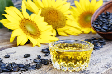 Sunflower oil and sunflower seeds in a bowl on a wooden background near fresh sunflower flowers. Organic and eco food.