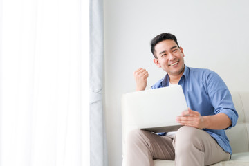 Asian handsome man working with laptop computer   in living room happy and smile face