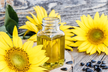 Sunflower oil in a glass jar with seeds and fresh flowers on a wooden background. Healthy foods and...
