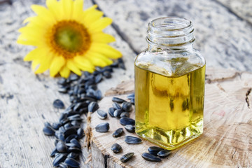 Organic sunflower oil in a glass jar with seeds and fresh flowers on a wooden background. Healthy foods and fats.