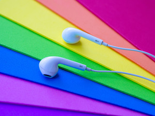 White wired headphones, headset on a multi-colored rainbow background (lgbt). Musical day
