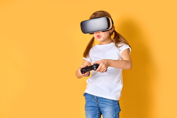 Girl experiencing VR headset vs joystick game on yellow background. Surprised emotions on her face. Child using a gaming gadget for virtual reality. Futuristic goggles at young age. Virtual technology