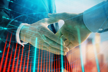 Double exposure of financial graph on cityscape background with two businessman handshake. Concept of stock market deal