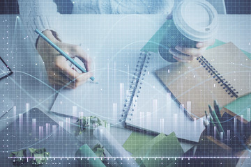 Financial forex graph displayed on hands taking notes background. Concept of research. Multi exposure