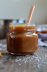 Open jar of salted caramel sauce over a rustic table. Selective focus with blurred background.