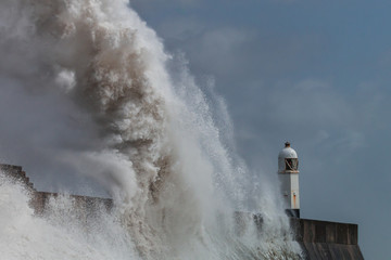 Huge ocean waves crashing into a sea wall and lighthouse (Porthcawl, South Wales, UK)