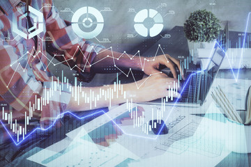 Double exposure of stock graph with businessman typing on computer in office on background. Concept...