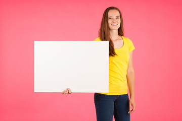 Fototapeta na wymiar Young woman in yellow t shirt holds blank banner for advertisment over vibrant pink background