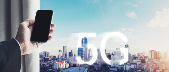 Hand holding mobile smart phone, with 5G internet wireless signal in the city