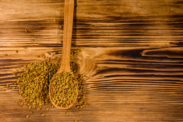 Spoon with fenugreek seeds on wooden table. Top view