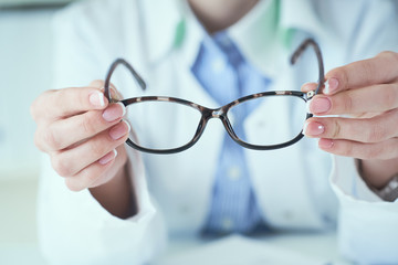 Female optician hands giving new glasses to customer for testing and trying close-up. Eye doctor with client comparing spectacles and choosing lenses in store.