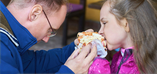 Father and daughter eat a hot dog. A man and a girl originally eat hot dog. Funny eating burger.