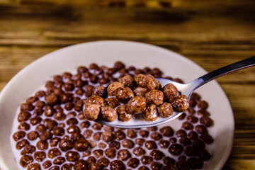 Ceramic plate with chocolate cereal balls in milk on wooden table