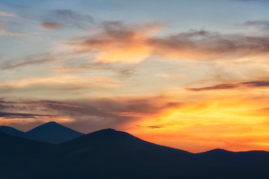 Background of bright orange sky at sunset. Mountain silhouettes. © imartsenyuk