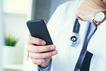 Male doctor in white coat is using a modern smartphone device with touch screen. Doctor hands with mobile phone.