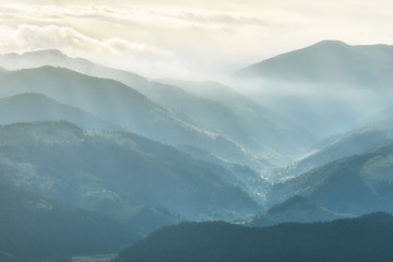 View of Carpathian mountain range with visible silhouettes through the colorful fog.