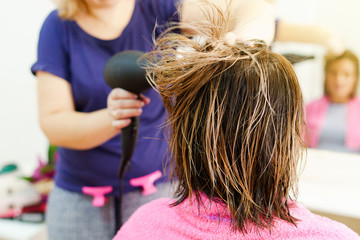 Professional female hairdresser drying woman's hair styling using blow dryer at the hairdressing...