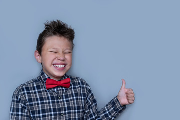 Young boy giving thumbs up portrait on violet background. Child enjoying, approving of something. Happy kid in red bowtie and checkered shirt giving likes. Fun, cheerful pastime, Dentistry concept