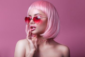 Close-up portrait of woman in sunglasses with bright colored pink hair and make-up on pink. Professional coloring