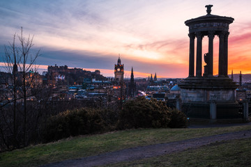 Edinburgh Skyline from Calton Hill at Dusk. A monument and a gravel path are visible in foreground.
