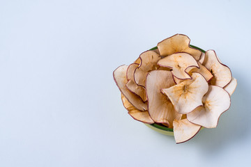 Dried apple chips in a bowl over light blue background.
