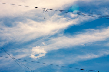 blue sky with white feathery clouds and intersecting wires
