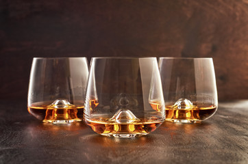 Three crystal glasses of whiskey on a wooden table.