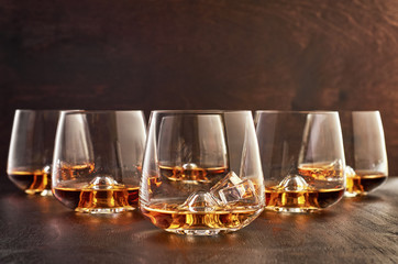 A set of six glasses of whiskey on a wooden table. In the foreground-a glass of whiskey with ice.