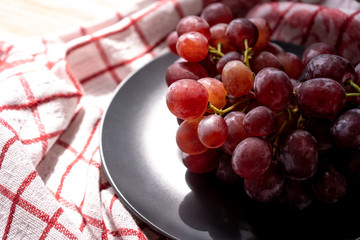 Bunch of ripe purple grapes in a bowl on the white and red napkin on a wooden background in the sun. Close-up. Top-side view