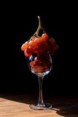 Bunch of ripe purple grapes in a wine glass on a wooden table in the sun. Vertical. Side view