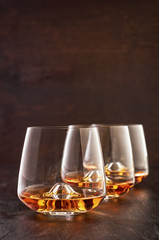 Three crystal glasses of whiskey on a wooden table.