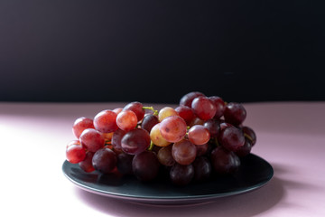 A bunch of ripe purple grapes on the grey plate on a pink background in the sun. Side view. 