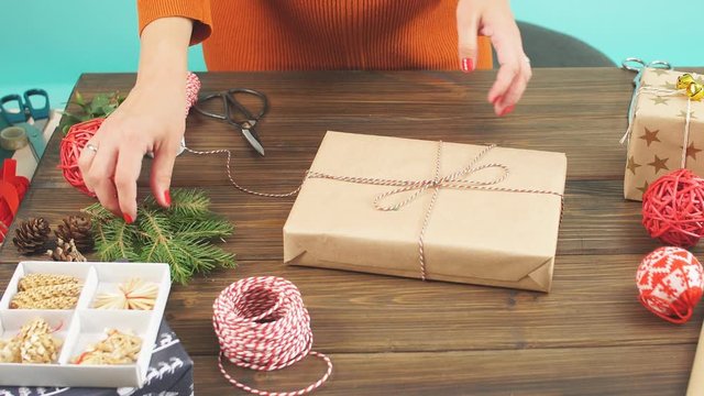 Christmas flatlay of unready hand crafted gift box on rustic wooden table with rolls of craft and colour wrapping paper, pine cones, fir branches and decor elements.