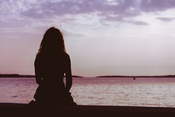 woman silhouette sitting on the beach looking at sunset over the sea