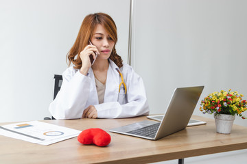 Medicine young Asian female doctor talking on the phone on workplace in hospital office. Health care and medical concept.