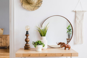 Sunny boho interiors of apartment with  mirror, dressing table, table lamp, flowers, plants, rattan...