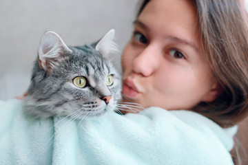 Beautiful woman at home kissing and hug her lovely fluffy cat. Gray tabby cute kitten with green eyes. Friend of human. Good sunny morning.