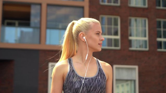 Young, attractive and sporty blond girl in sportswear listening to the music outdoor. Healthcare and lifestyle.