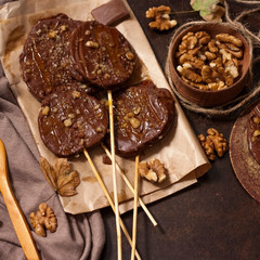 Slices of apples in chocolate, caramel glaze and walnuts on skewers on a dark background