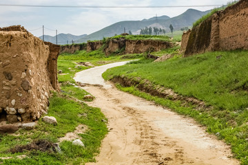 Fototapeta na wymiar A dirt road winds up a small hill around a mud wall in rural China with a power line running across the top