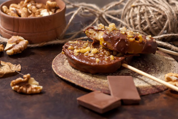 Slices of apples in chocolate, caramel glaze and walnuts on skewers on a dark background