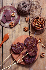 Slices of apples in chocolate, caramel glaze and walnuts on skewers on a dark background