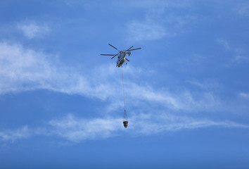 Fire fighting helicopter with waterbag on his way to combat the  fire